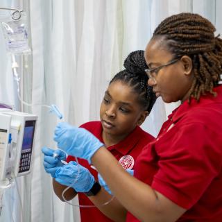 Two women wearing red shirts preparing an IV